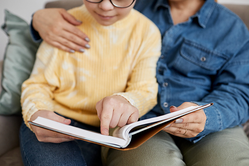 Close up of young girl with Down syndrome reading book with loving mother at home
