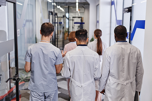 Rear view of several young intercultural medical workers in lab coats and uniform discussing working points on the move