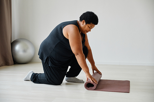 Side view portrait of black senior woman unrolling yoga mat while exercising in studio, copy space