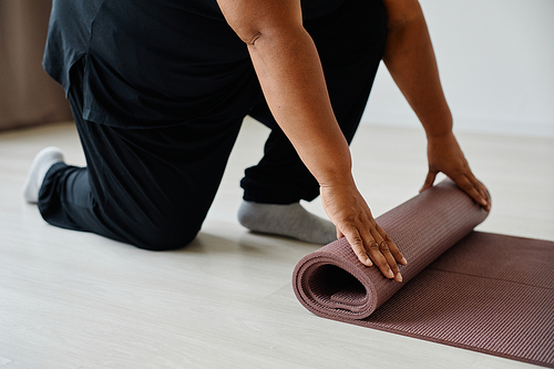 Close up of black senior woman unrolling yoga mat while exercising in studio, copy space