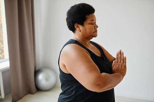 Side view portrait of black senior woman meditating with eyes closed while doing yoga indoors, copy space