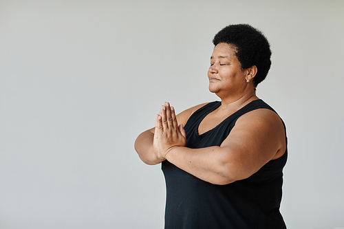 Minimal side view portrait of black senior woman meditating with eyes closed while doing yoga indoors, copy space