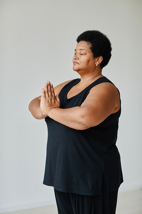 Vertical portrait of black senior woman meditating with eyes closed while doing yoga indoors