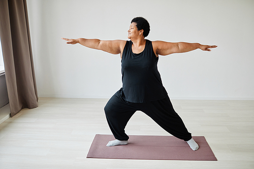 Minimal full length portrait of active senior woman doing yoga indoors and smiling, copy space