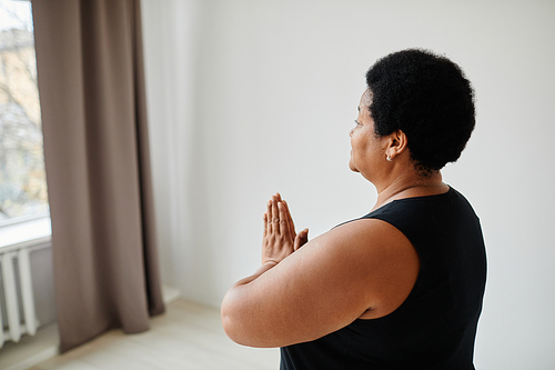Minimal side view portrait of black mature woman enjoying yoga indoors and looking at window, copy space