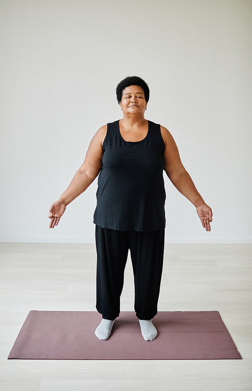 Vertical full length portrait of black senior woman enjoying yoga indoors