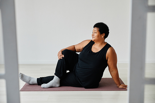 Full length portrait of active senior woman enjoying yoga indoors on mat