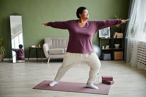 Full length portrait of active senior woman doing yoga at home and enjoying workout indoors, copy space