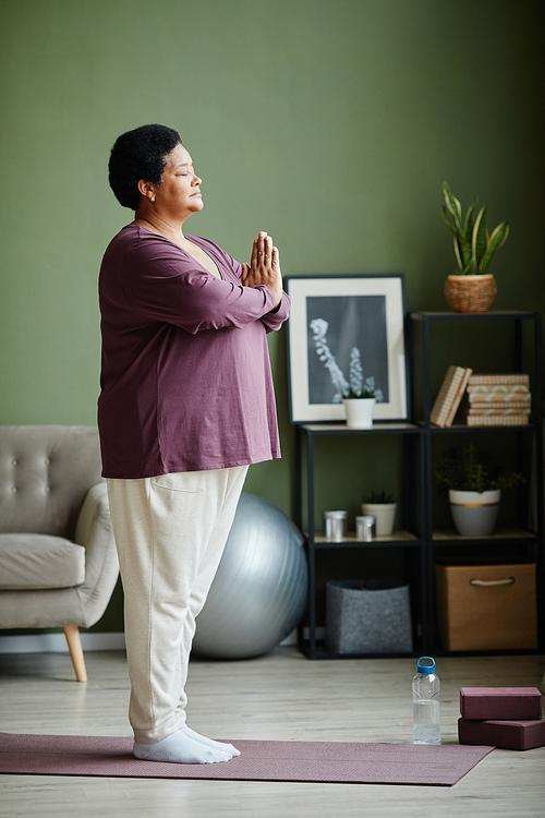 Side view full length portrait of active senior woman doing yoga at home and practicing balance