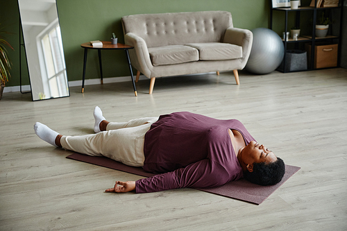 High angle view at black senior woman laying on yoga mat and relaxing while enjoying yoga at home
