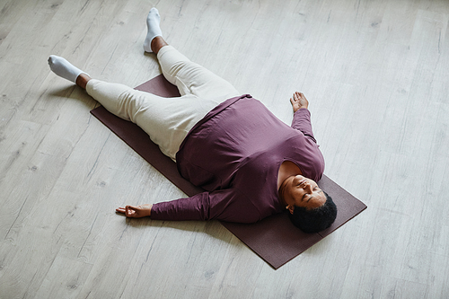 Top view portrait of black senior woman lying on floor with eyes closed while enjoying relaxation exercise