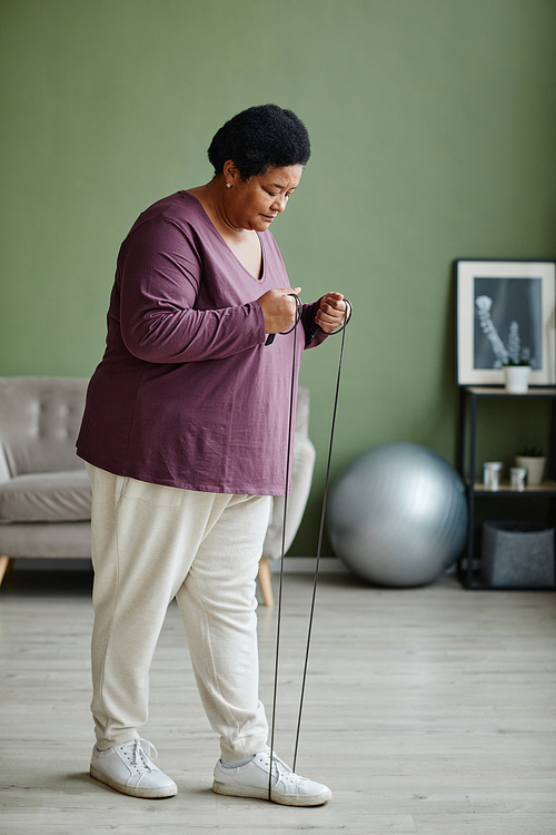 Vertical full length portrait of black senior woman adjusting jumping rope for home workout