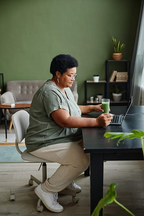 Vertical side view portrait of black senior woman using laptop at home for online shopping