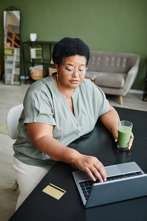 Vertical portrait of black senior woman using laptop at home and shopping online or paying taxes
