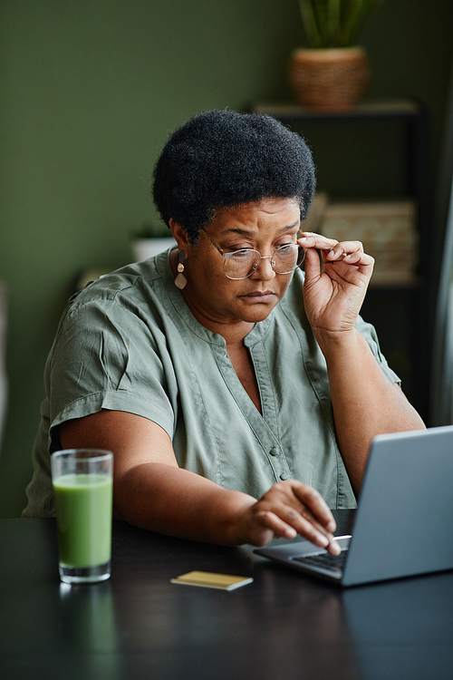 Vertical portrait of black senior woman using laptop and shopping online from home