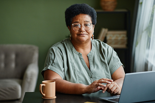 Portrait of mature black woman using laptop while working from home or shopping online, copy space