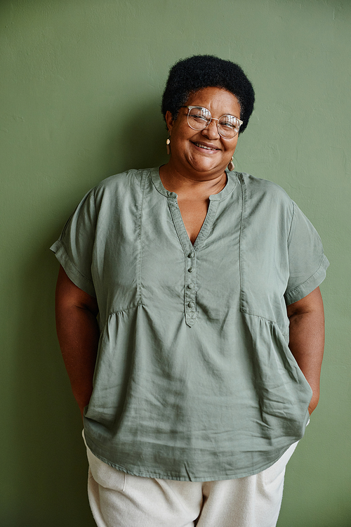 Vertical portrait of black senior woman wearing glasses and smiling at camera while standing against green background