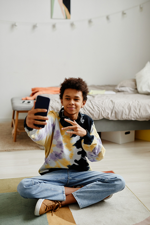 Full length portrait of smiling black teenager with smartphone filming video for social media at home