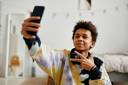 Portrait of smiling black teenager with smartphone filming video for social media at home