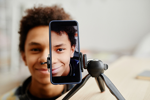 Half face portrait of smiling black teenager filming video for social ,media, focus on smartphone screen, copy space