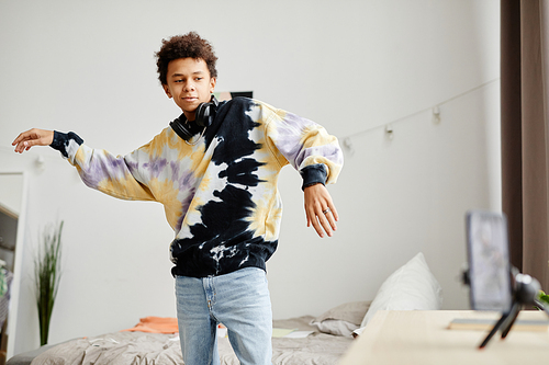Portrait of black teenage boy wearing tie dye shirt filming dance video to latest trend on social media, copy space
