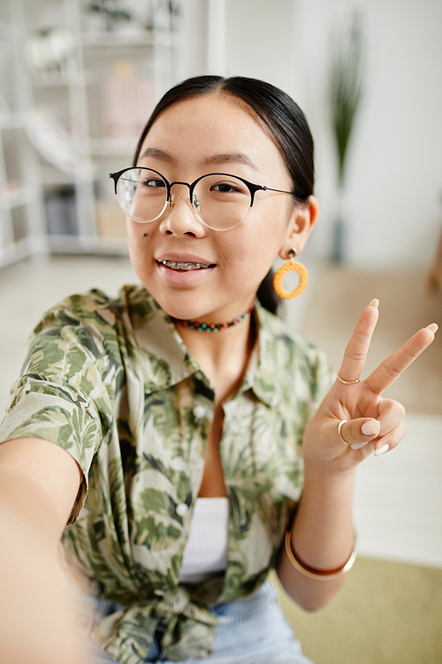 Vertical POV portrait of trendy teenage girl with braces smiling at camera and taking selfie