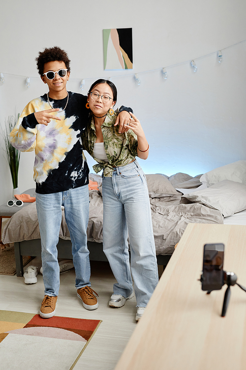 Full length portrait of two gen Z teenagers filming video for social media, boy and girl posing for smartphone recording