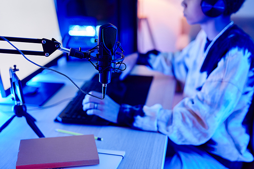 Close up of teenager playing video games and streaming live, focus on professional microphone, scene lit by neon