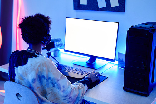 Back view of teenage boy playing video game on PC and streaming live in blue neon light with white screen mockup, copy space