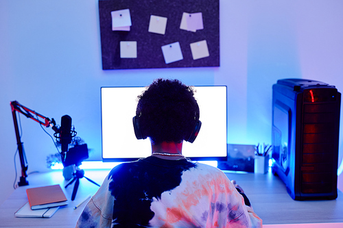 Minimal back view of teenage boy playing video game on PC and streaming live in blue neon light with screen mockup, copy space