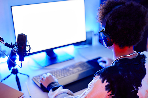 Closeup of teenage boy playing video game and streaming live in blue neon light with white screen mockup, copy space