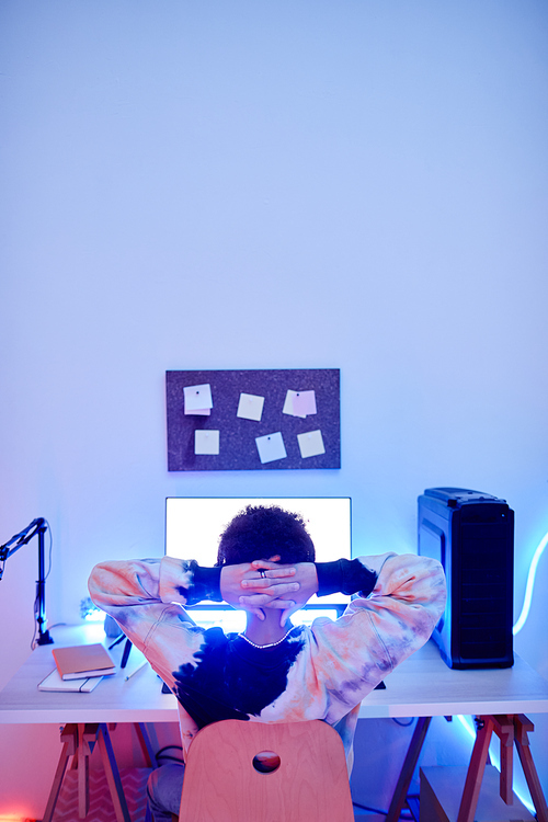 Minimal back view of teenager watching videos on PC with blue neon light, copy space