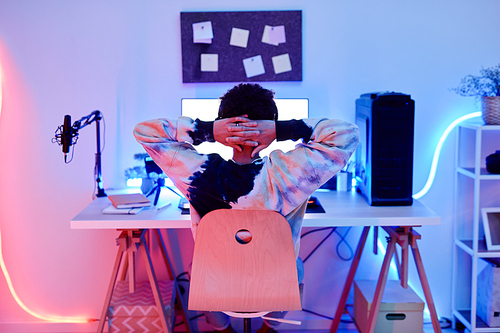 Back view of teenage boy watching videos on internet at night with blue neon lighting, copy space