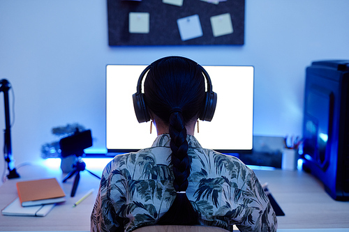 Back view of teenage girl playing video games at night with blue neon lighting, copy space