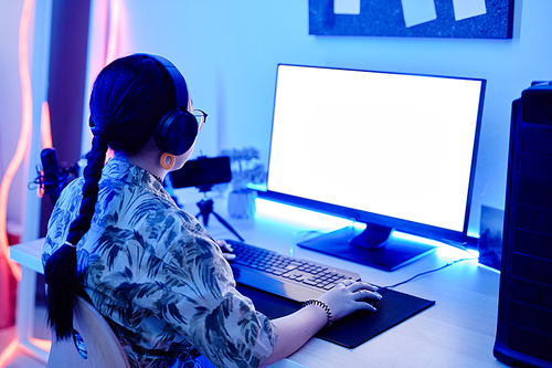 Portrait of teenage girl playing video games at night with computer screen mockup in blue neon lighting, copy space