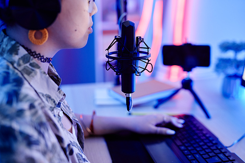 Closeup of teenage girl playing video game on PC and speaking to microphone while streaming live in blue neon light