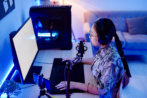 High angle portrait of young teenage girl recording podcast at night with blue neon lighting, copy space