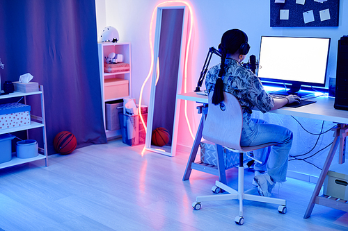 Wide angle angle portrait of young teenage girl recording podcast at night in room with blue neon lighting, copy space