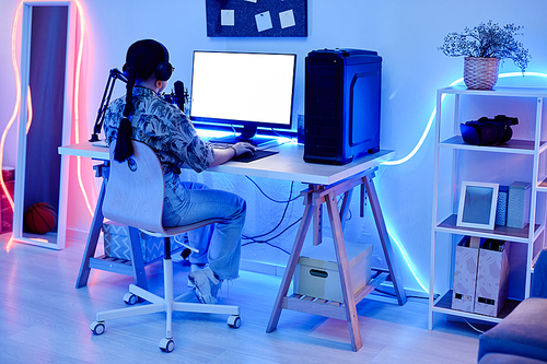 Full length portrait of young teenage girl playing video games at night in room with blue neon lighting, copy space