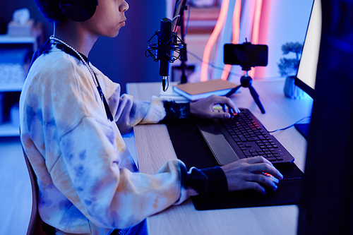 Cropped portrait of young teenage boy recording podcast at night in room with blue neon lighting, copy space