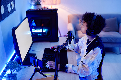 High angle portrait of black teenage boy playing video games at night in room with blue neon lighting, copy space
