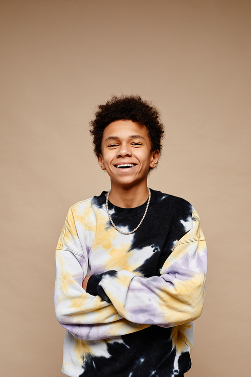 Vertical portrait of African American teenage boy wearing tie dye shirt and smiling at camera over beige background