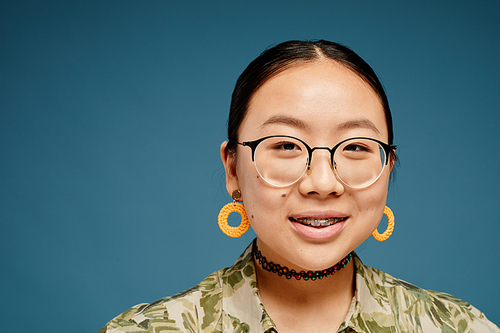 Minimal portrait of Asian teenage girl wearing braces and looking at camera over blue background, copy space