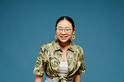 Minimal portrait of Asian teenage girl wearing eyeglasses and smiling over blue background, copy space