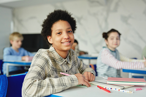 Portrait of smiling African American girl sitting at desk in school and looking at camera