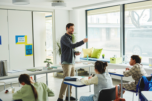 Wide angle view at smiling male teacher working with children in school classroom, copy space