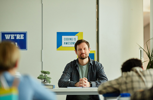 Wide angle view of bearded male teacher overseeing children doing test examination in school