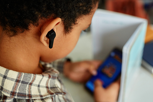 Close up of black kid listening to music during school class and hiding phone, copy space