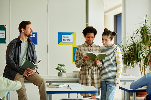 Portrait of two girls answering questions in school in front of classroom, copy space