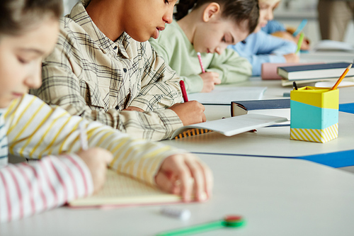 Close up of diverse group of children sitting in row and taking test in school classroom